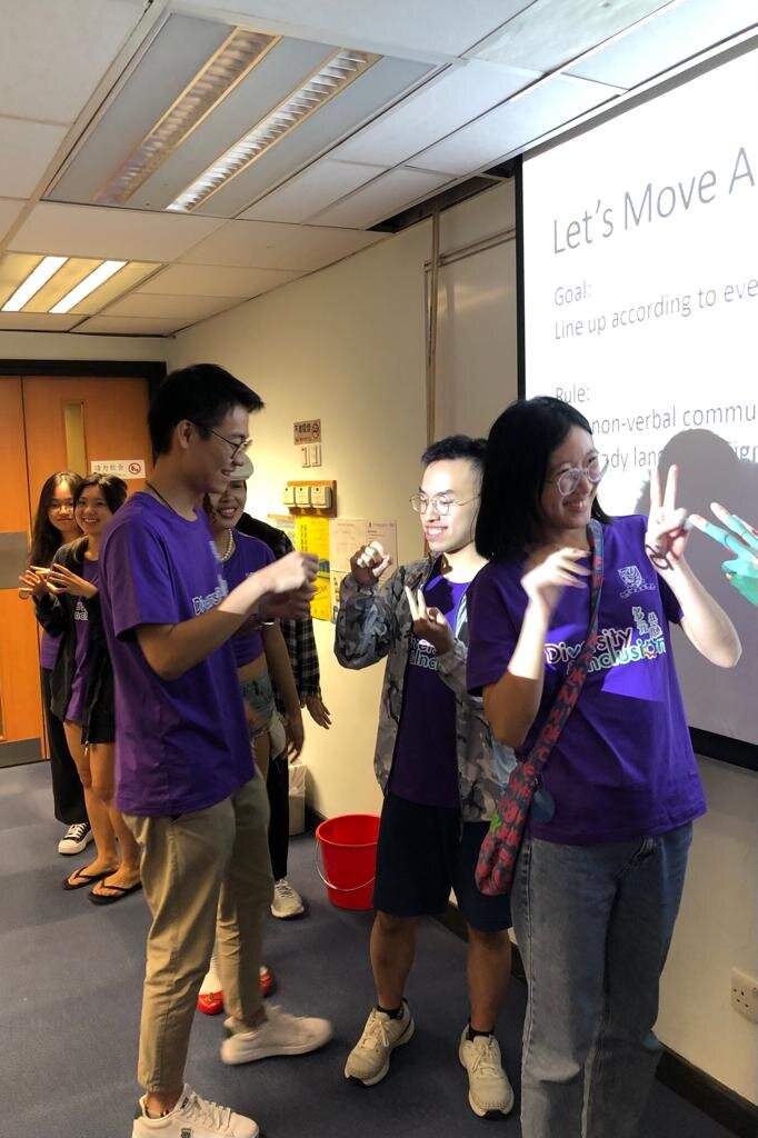 A group of ambassadors wearing purple 'Diversity & Inclusion' shirts are engaged in an ice-breaking game at the D&I Ambassador Programme Opening Ceremony. They are using gestures to find the right partner in the game.