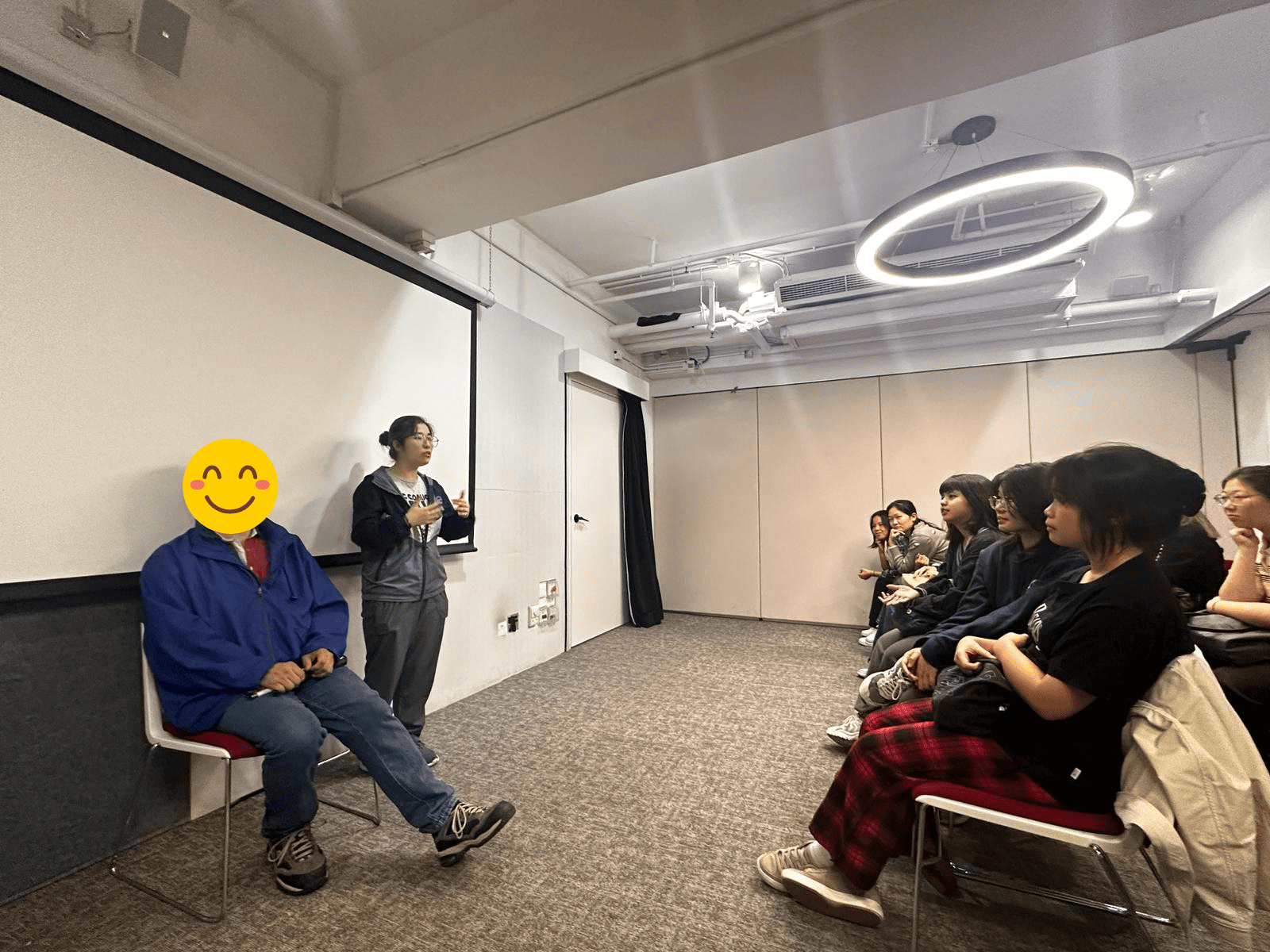 The participants are listening attentively to a visually impaired speaker, with a sign language interpreter standing next to him.