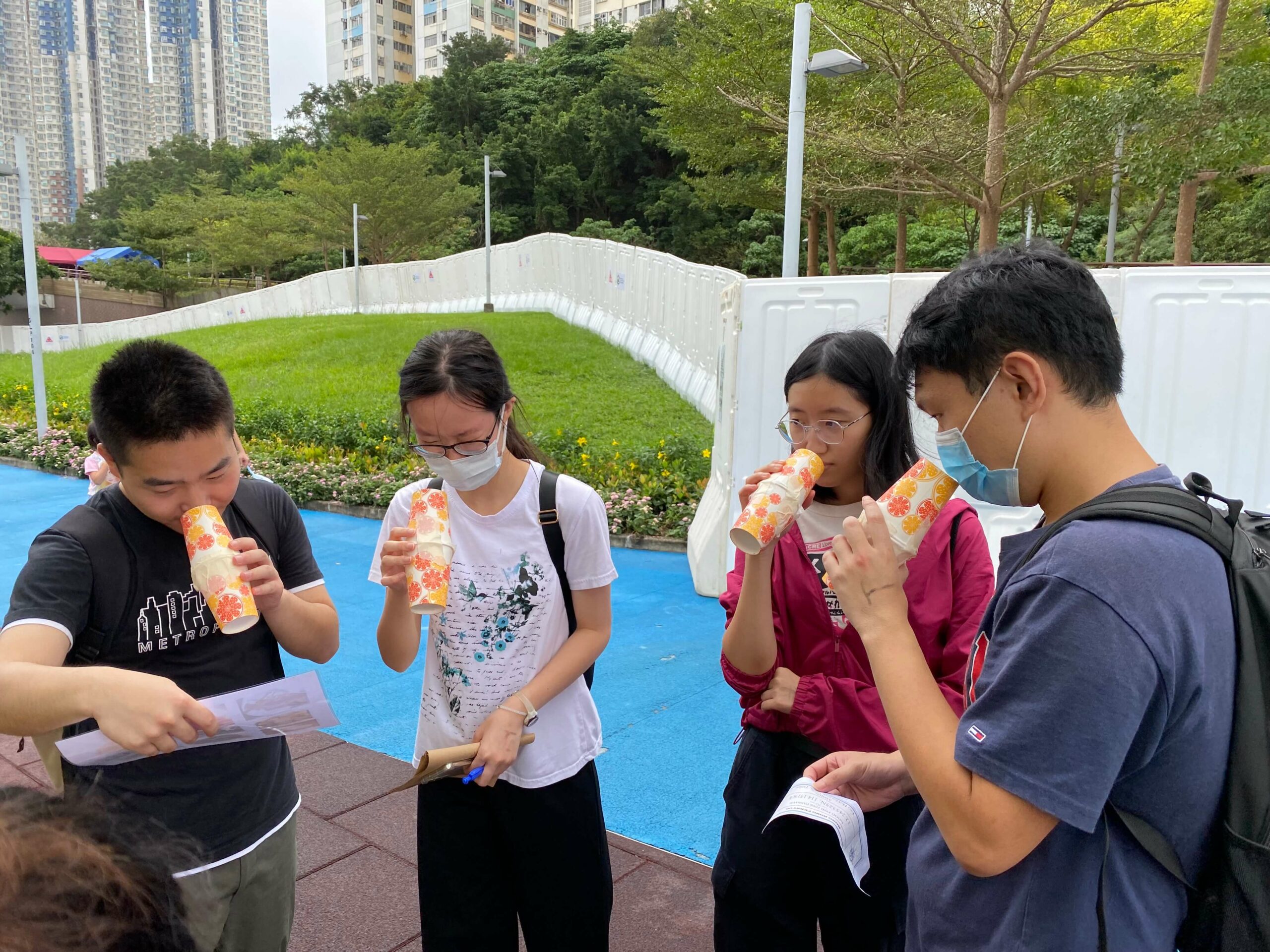 Four people stand outdoors holding colorful cups and gathered around.