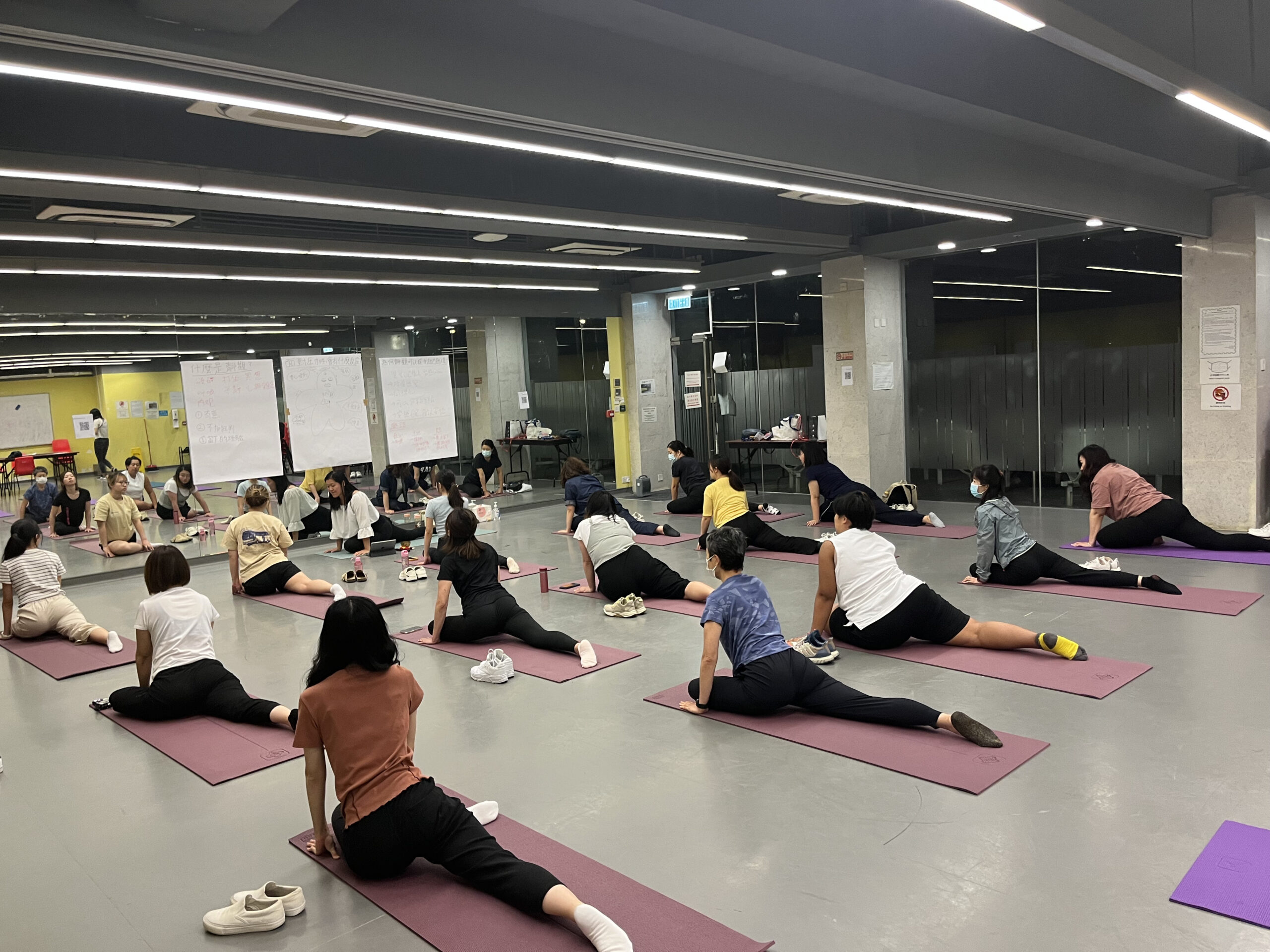 A group of people in a spacious room participating in a yoga workshop, each on a purple mat practicing various poses.