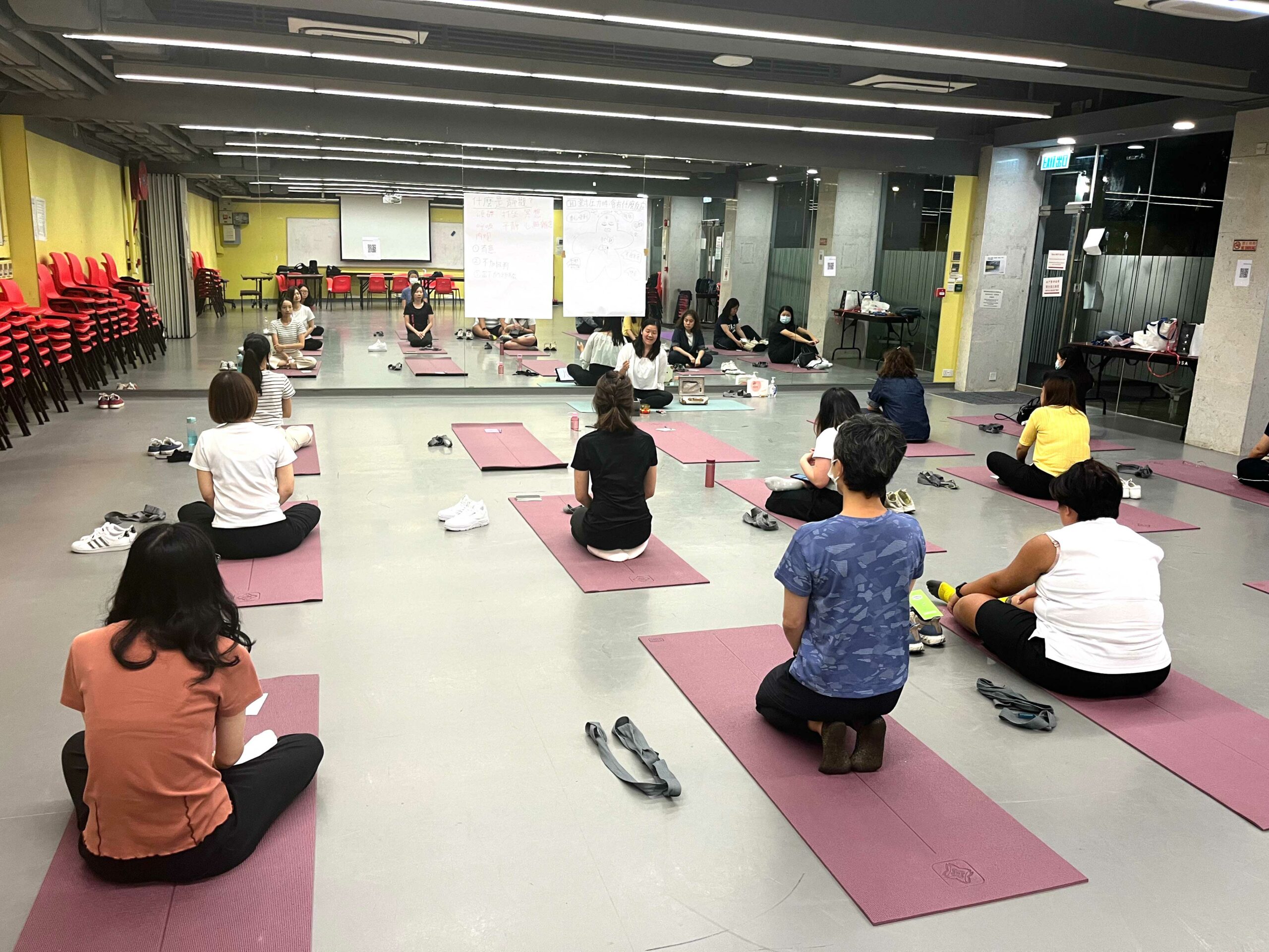 Participants follow an instructor's guidance while performing a pose on mats, emphasizing relaxation and fitness.