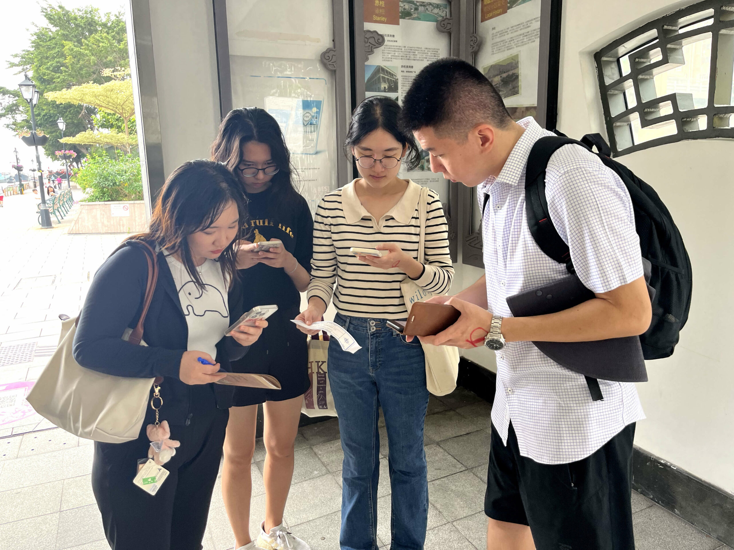 Four people are standing together, looking at their phones and holding papers. They are finding the clues for the next checkpoint.