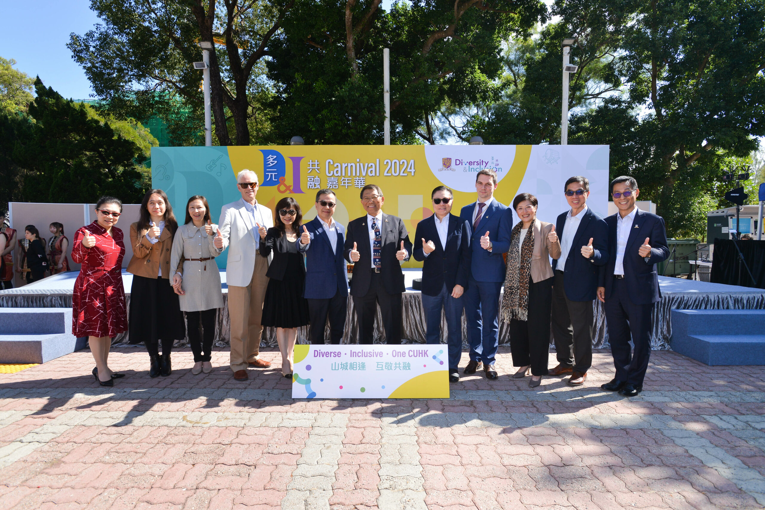 The guests stand in front of a "Carnival 2024" and "Diversity & Inclusion" stage backdrop. The sign reads "Diverse • Inclusive • One CUHK."