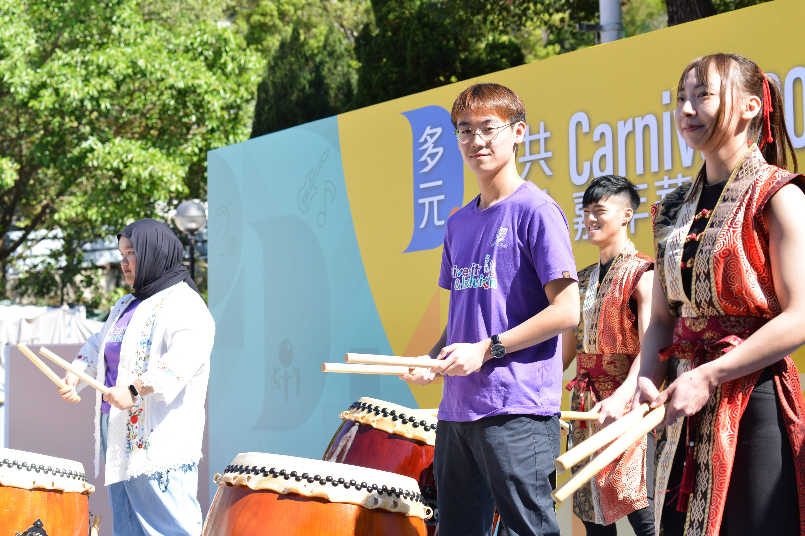 Performers wearing traditional attire and two D&I ambassadors on stage play traditional Japanese taiko drums.