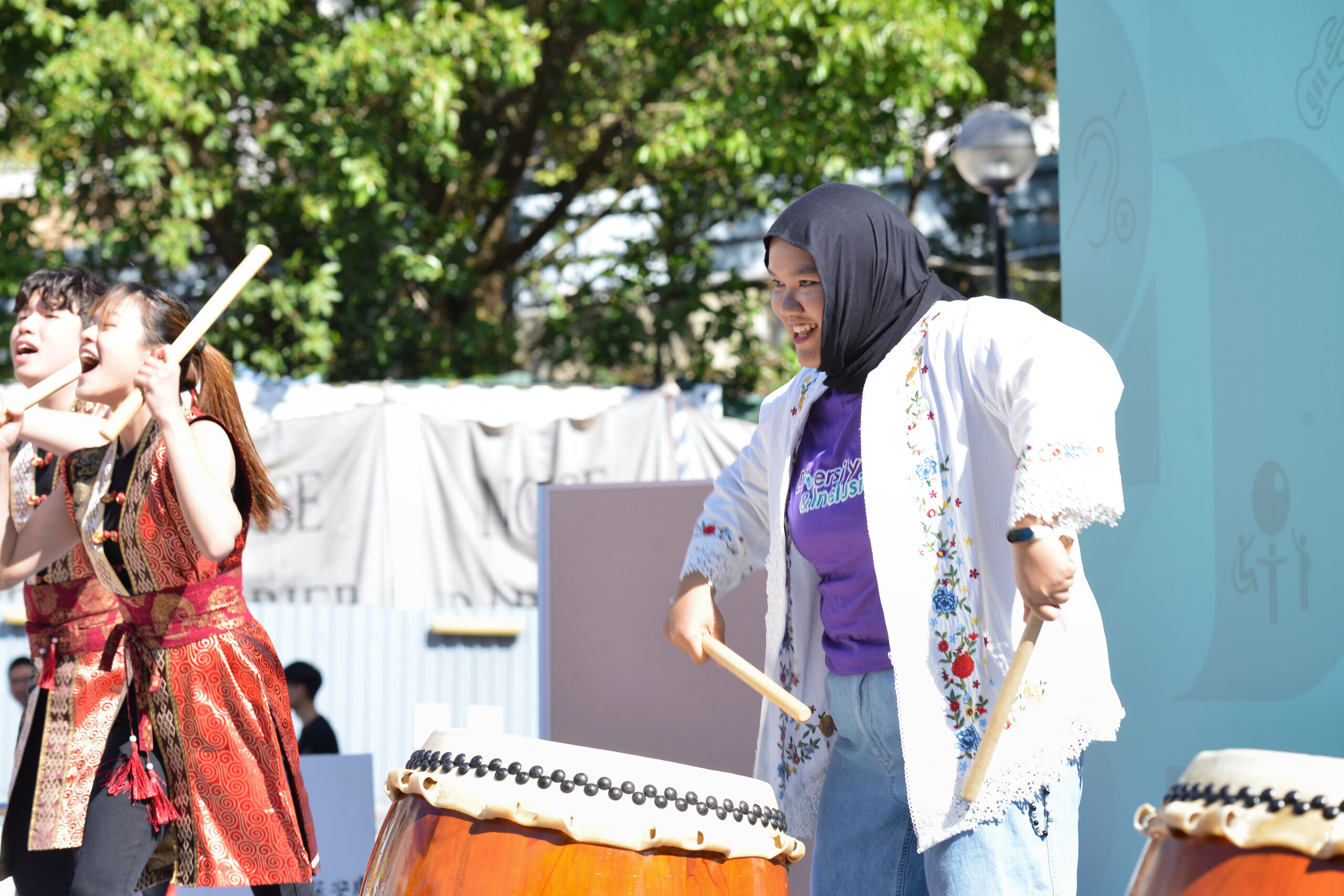 Performers wearing traditional attire and a D&I ambassadors on stage play traditional Japanese taiko drums.