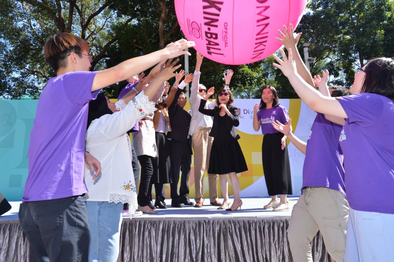 The guests and student ambassadors stand on an outdoor stage, reaching towards a large pink Kin-ball.