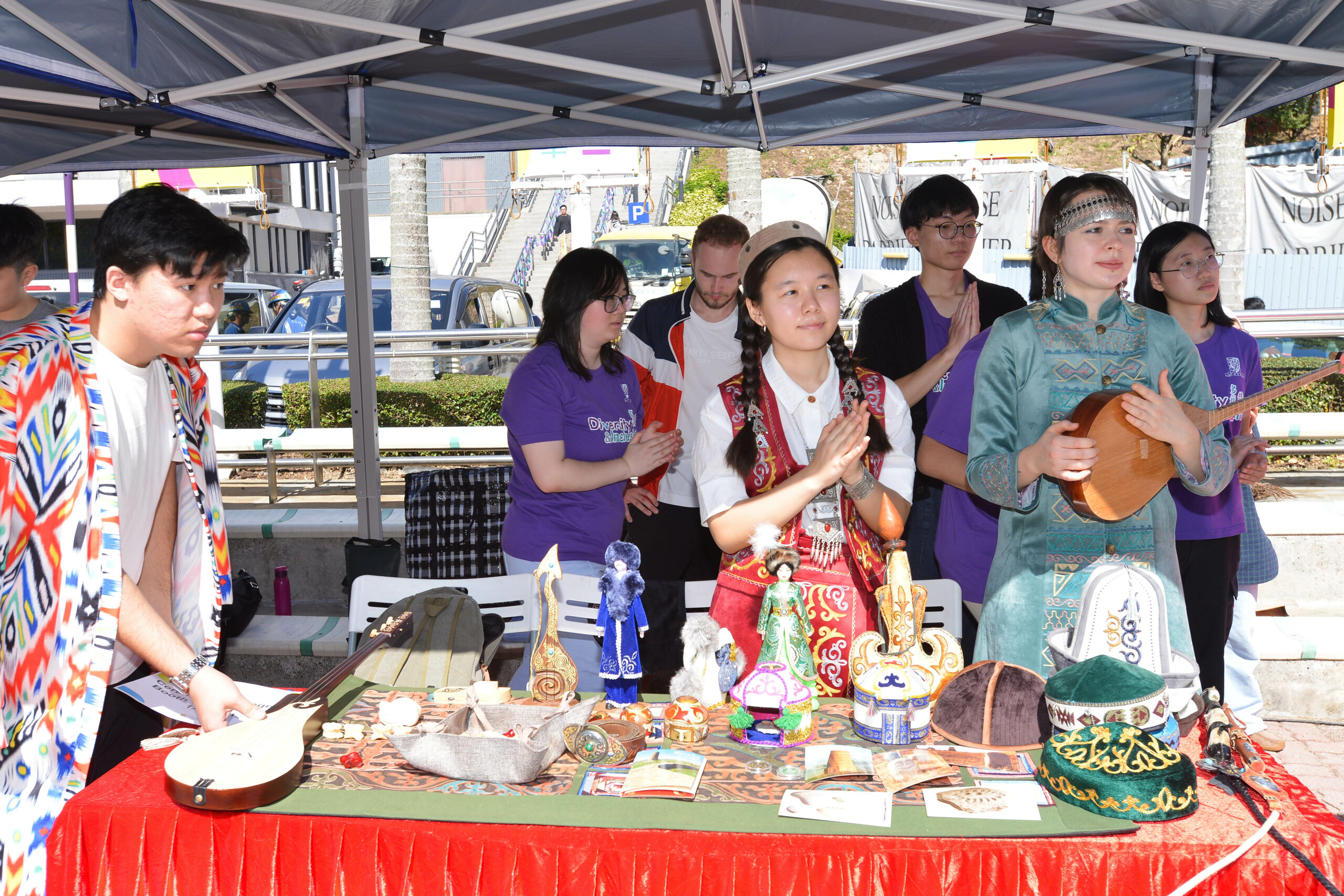 Students from Central Asian Association display cultural artifacts and instruments at an outdoor event under a tent.