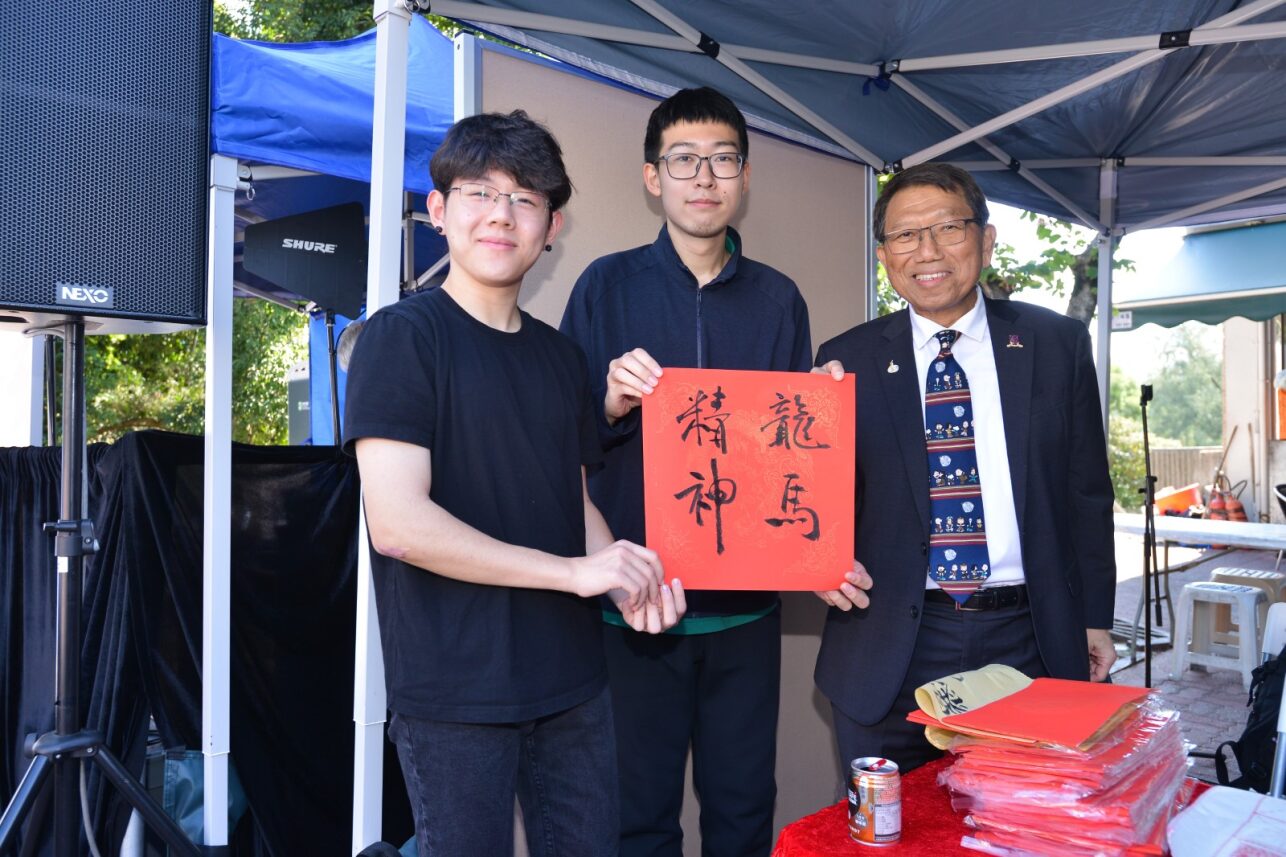 Prof. Rocky Tuan writes fai chun at the Mainland Undergraduate Association booth during D&I Carnival 2024, holding it with other two students.