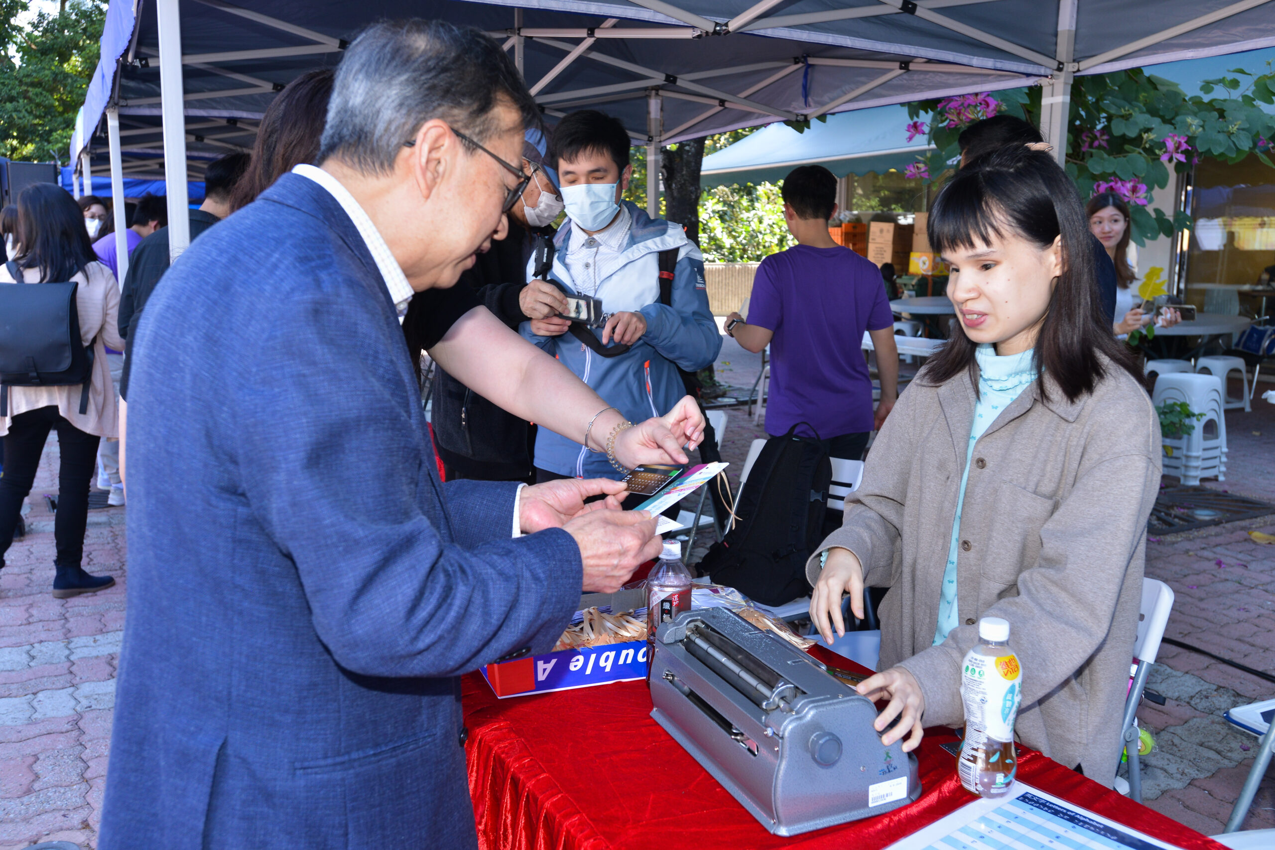 A guest is participating in a workshop on making braille bookmarks, assisted by a representative from The Ebenezer School and Home for the Visually Impaired.