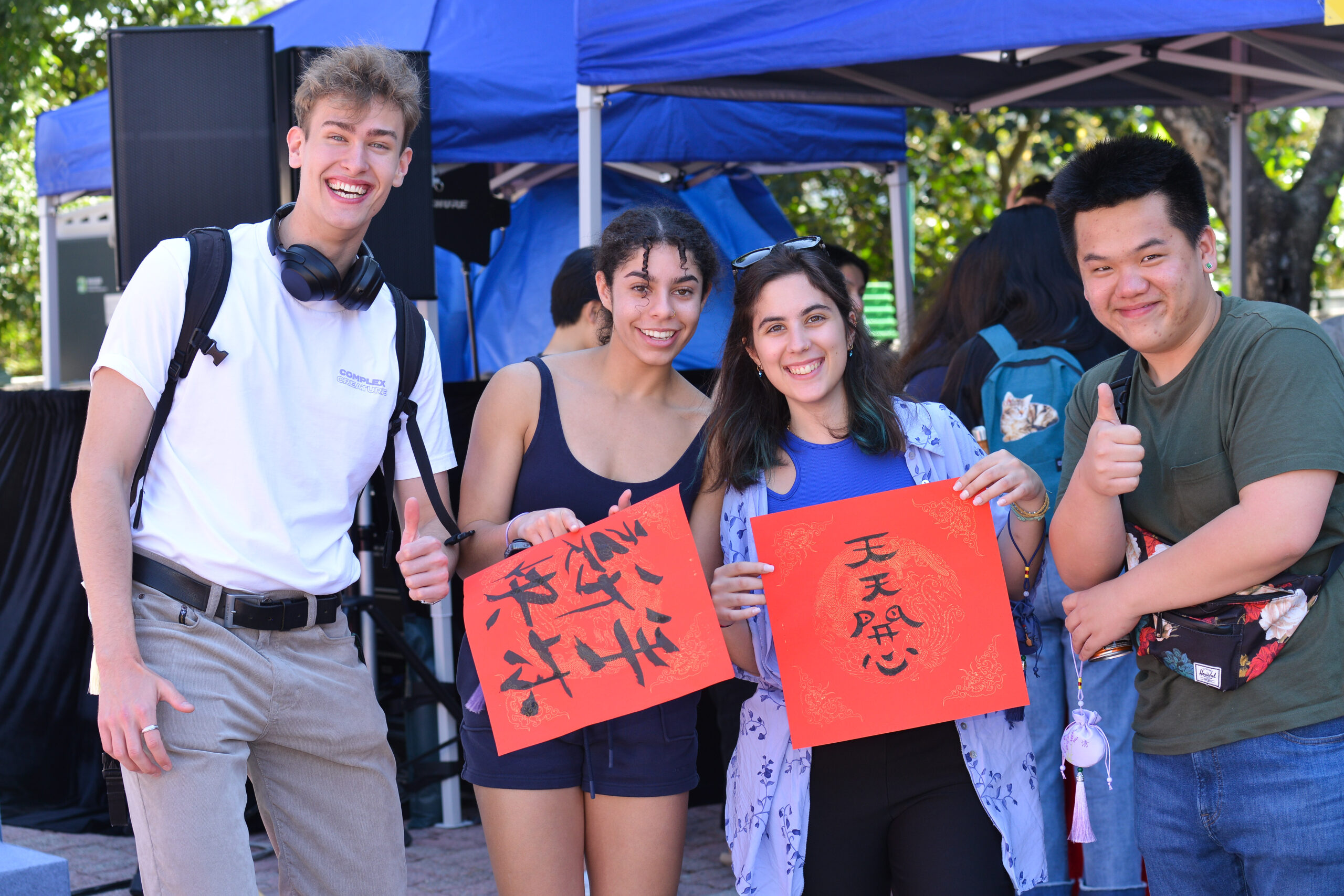 Four participants holding the fai chun they wrote at the workshop, with two of them giving thumbs-up gestures.