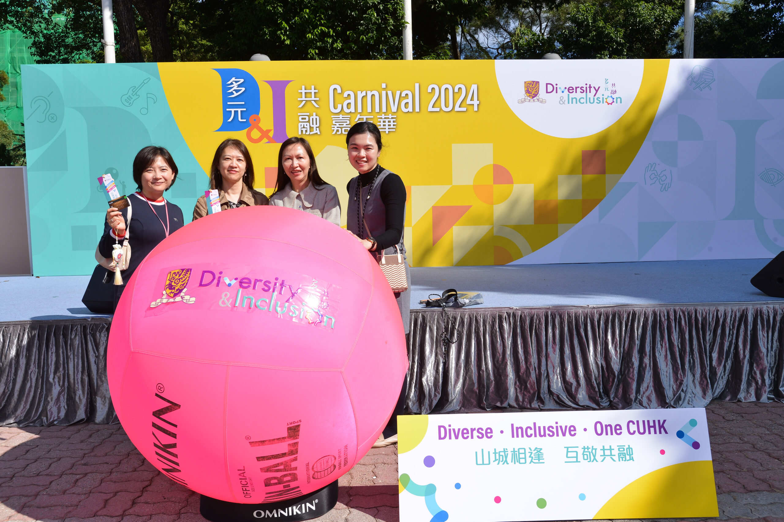 Group of four standing in front of the stage at D&I Carnival 2024 with a large pink ball labeled 'Diversity & Inclusion'