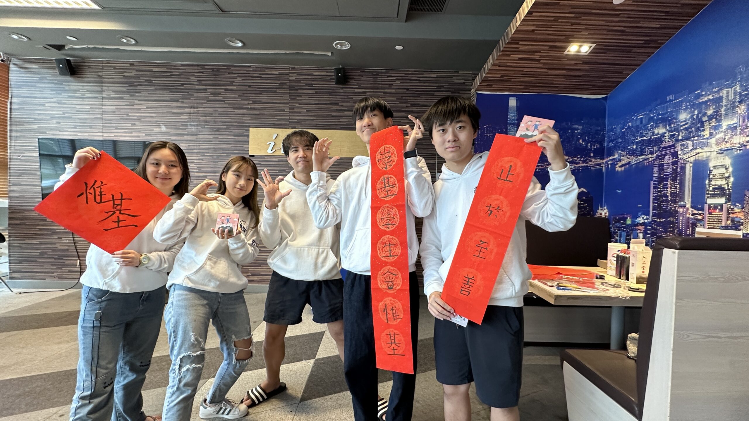 Five students standing indoors, each holding the fai chun they wrote during the workshop.