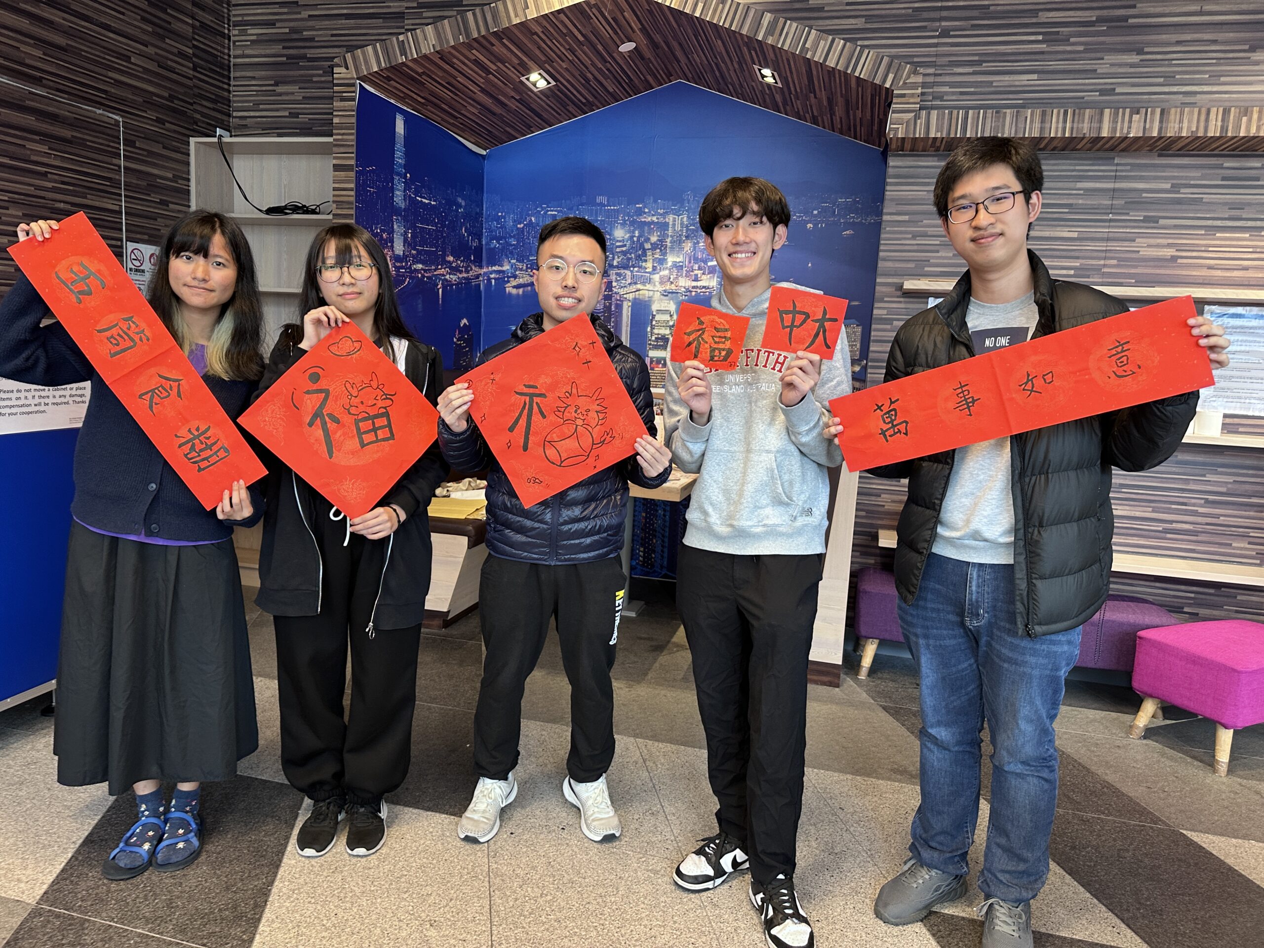 Five students standing indoors, each holding the fai chun they wrote during the workshop.