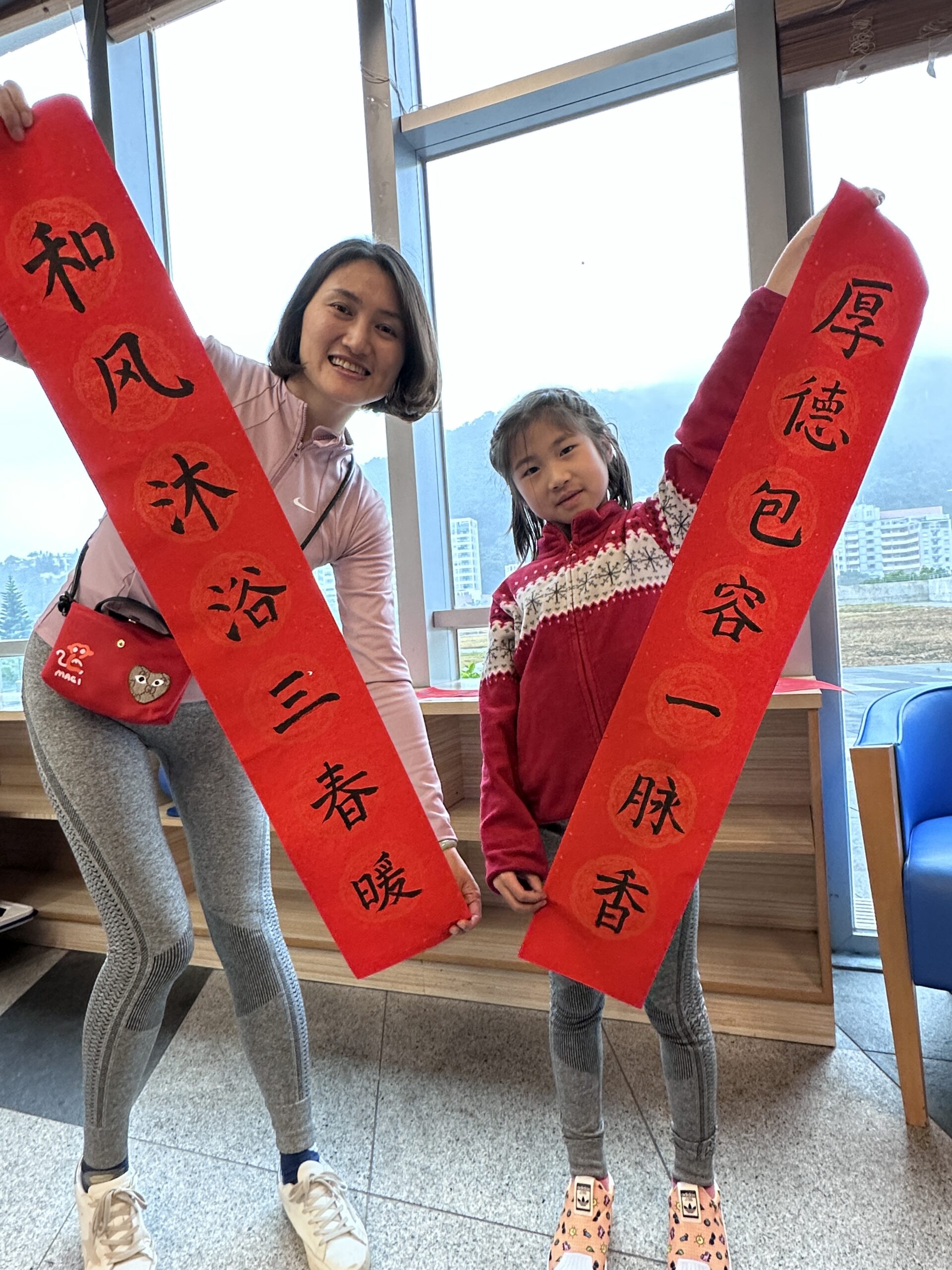 Mother and daughter hold fai chun with Chinese calligraphy.The scene captures their bonding and cultural celebration.