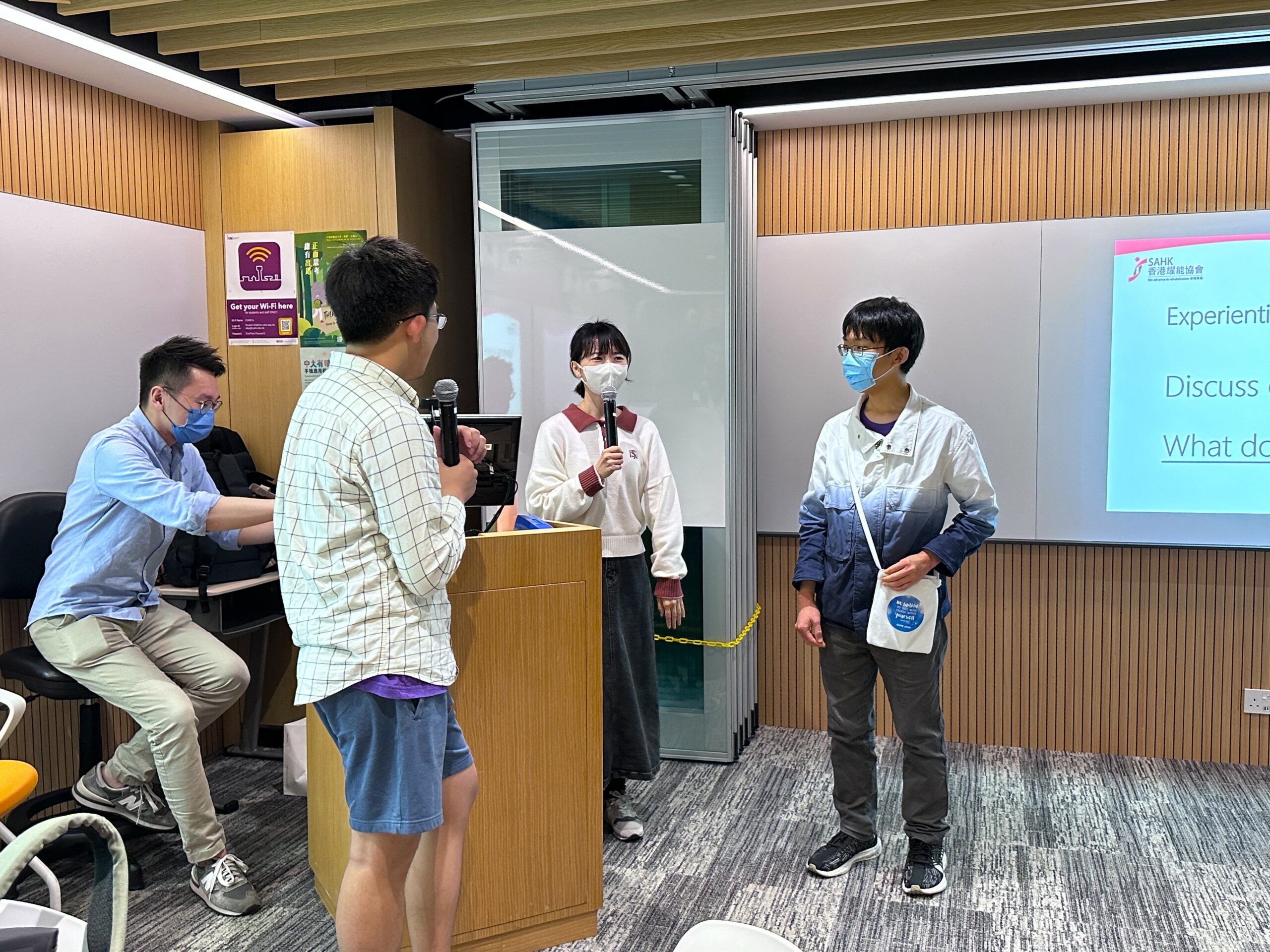 Two students participate in a role play session. One student stands behind a podium with a microphone, while the other stands beside them, engaging in the activity.