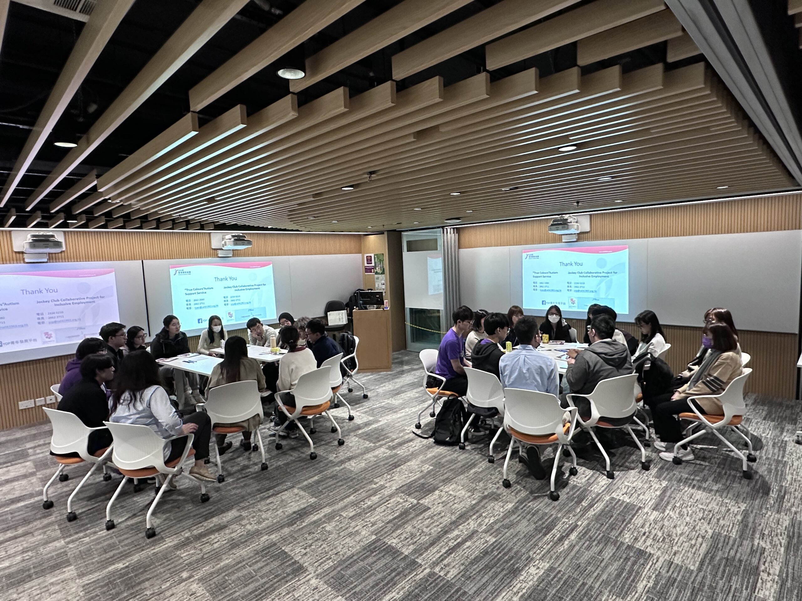 A group of people sits in a classroom or conference room, engaging in a group discussion about the difficulties faced by people with special educational needs (SEN).