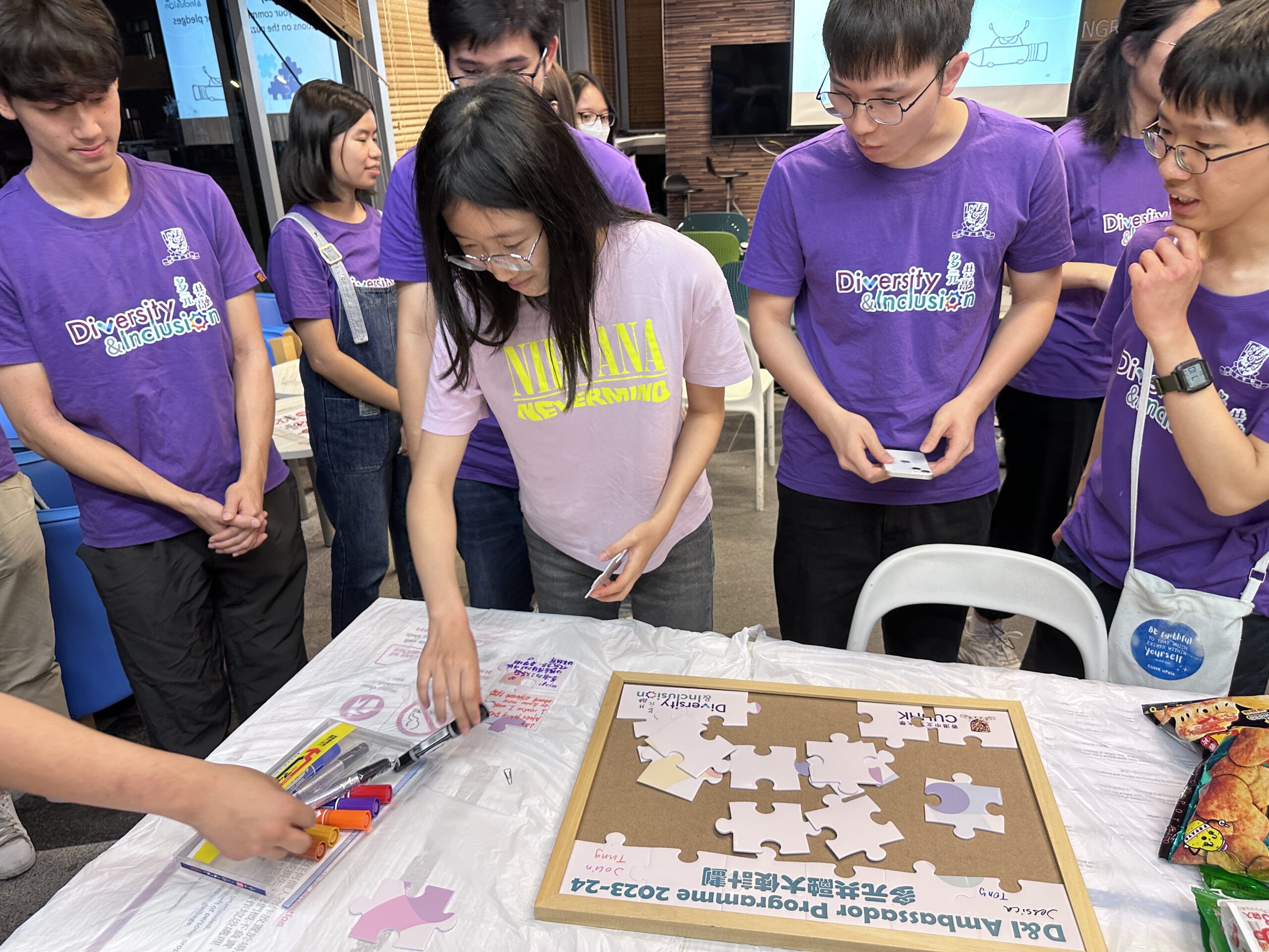 A group of ambassadors engages in an activity involving puzzle pieces around a table. They write down their commitment to diversity and inclusion.