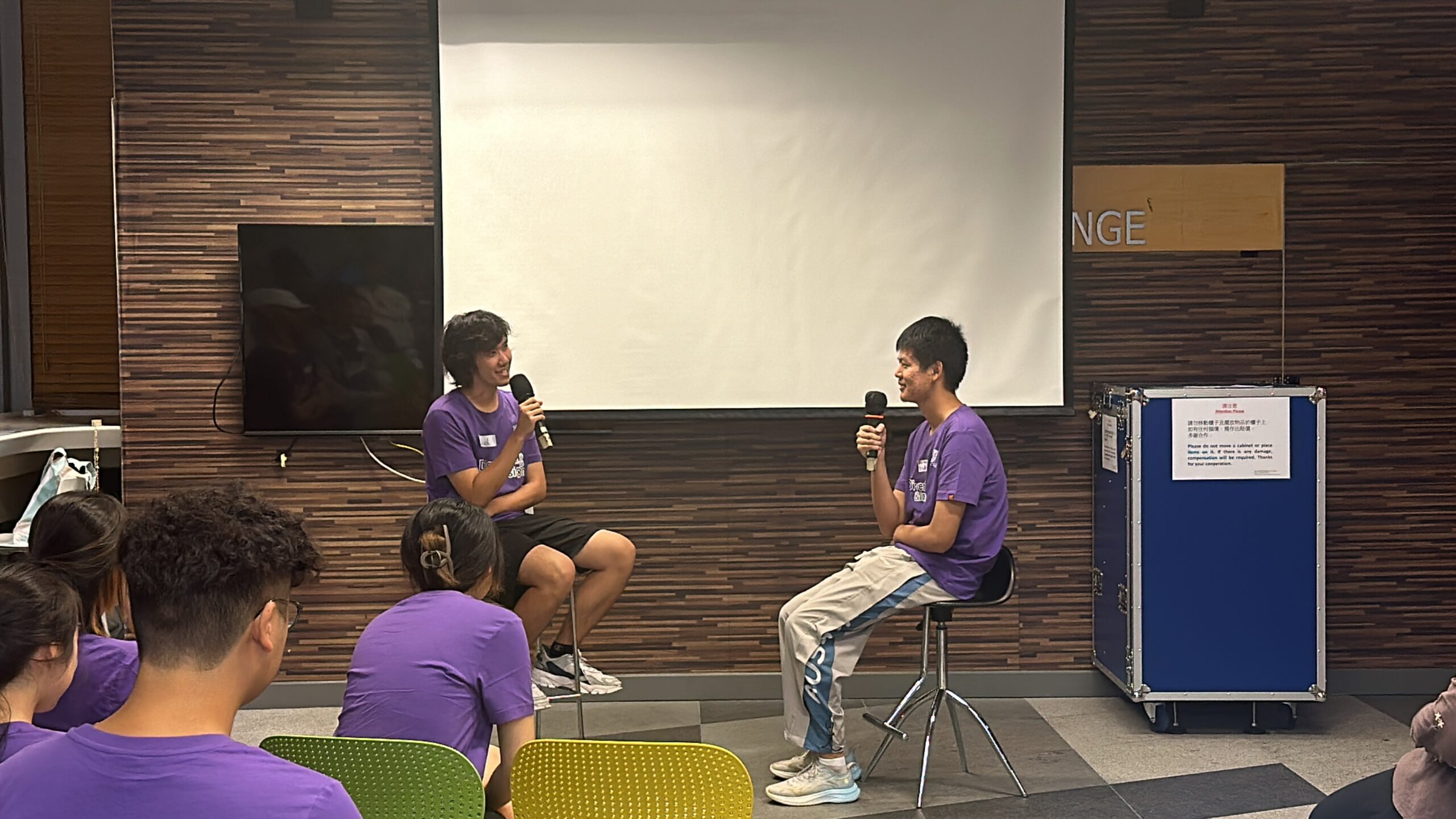 D&I ambassadors are engaging in a role play session, with two seated on stools at the front holding microphones.