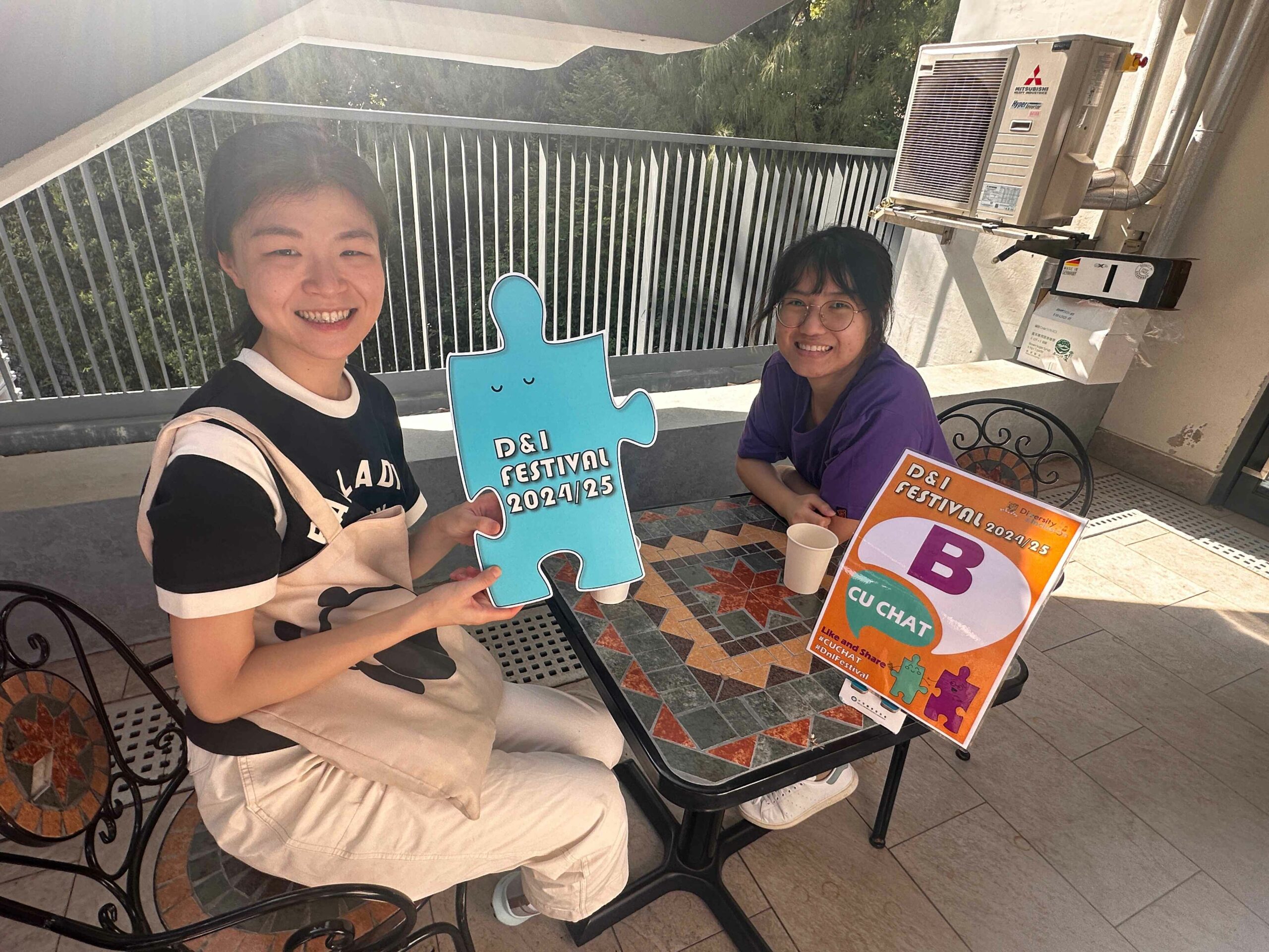 The D&I ambassador and a participant are holding colorful props promoting D&I festivals, smiling.