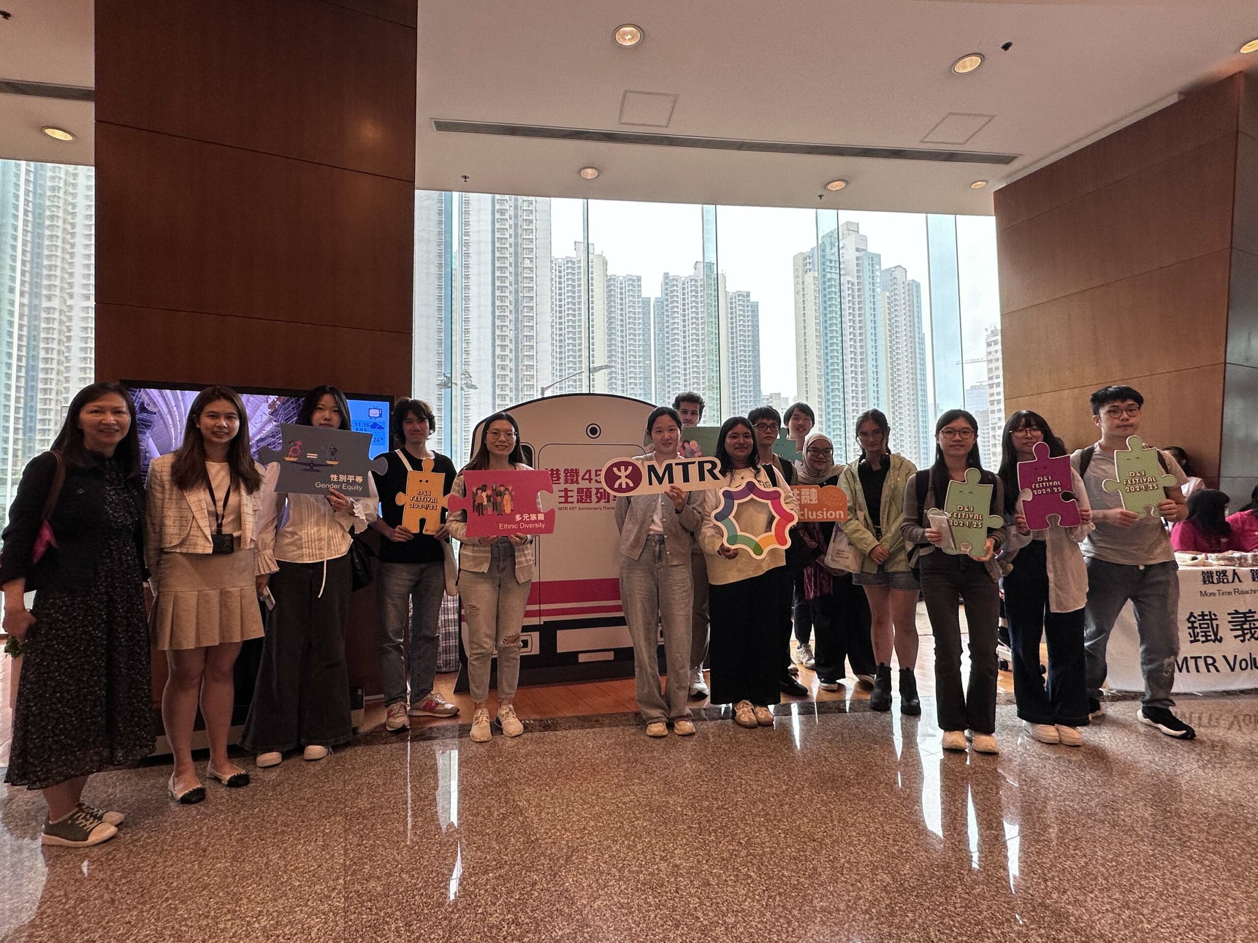 A group of participants standing next to a train-shaped backdrop, holding colorful props promoting diversity and inclusion, and taking a group photo.