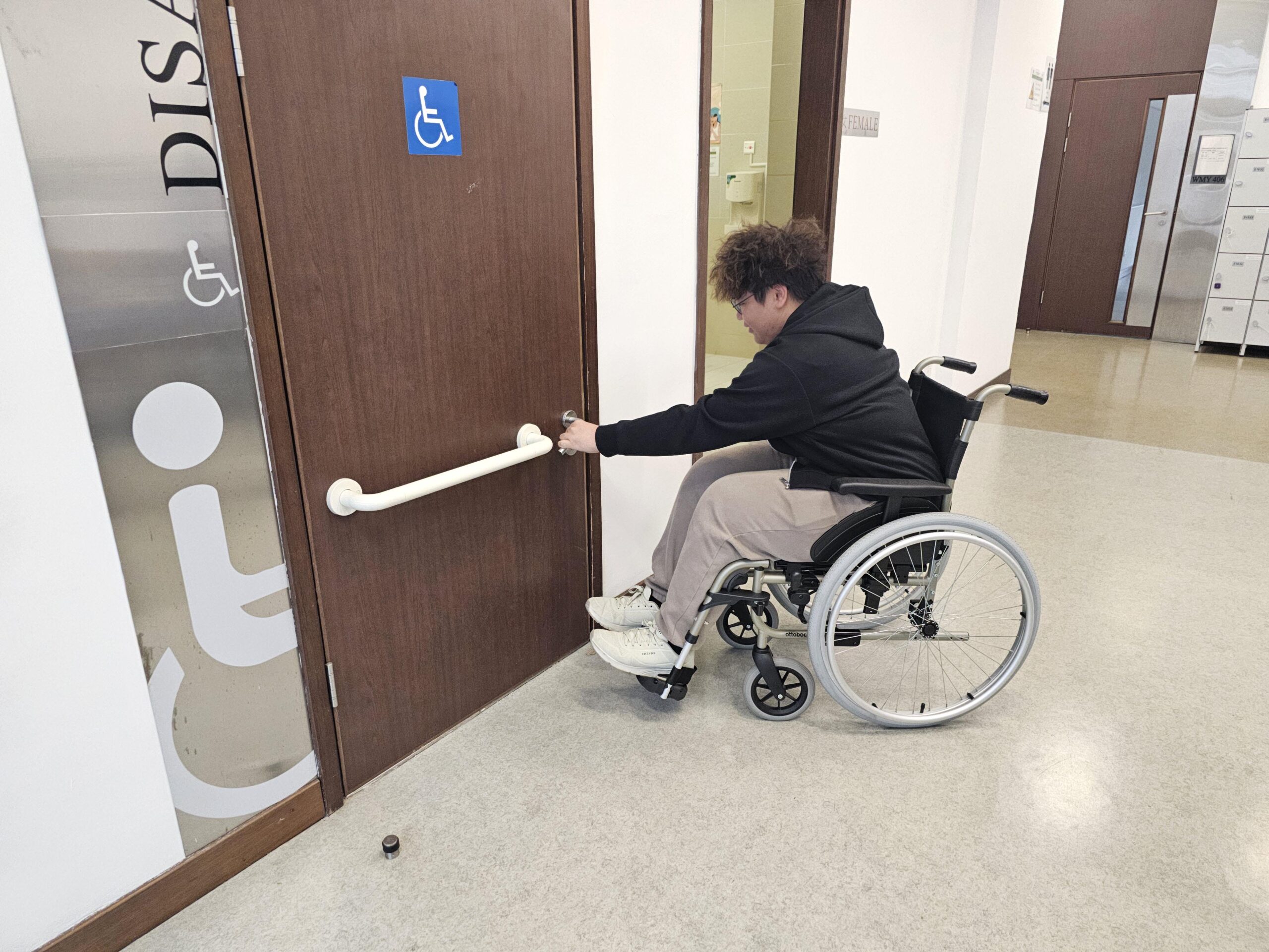 A D&I ambassador is seated in a wheelchair, attempting to open the door of an accessible toilet, experiencing firsthand the daily challenges faced by wheelchair users.